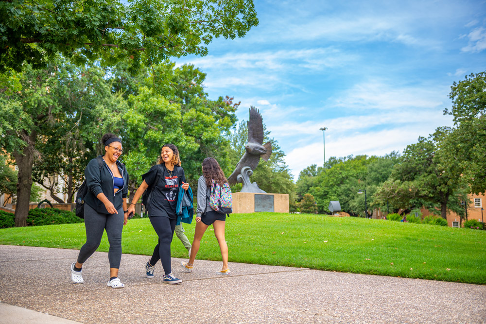 Students walking on campus near the eagle statue on sunny day